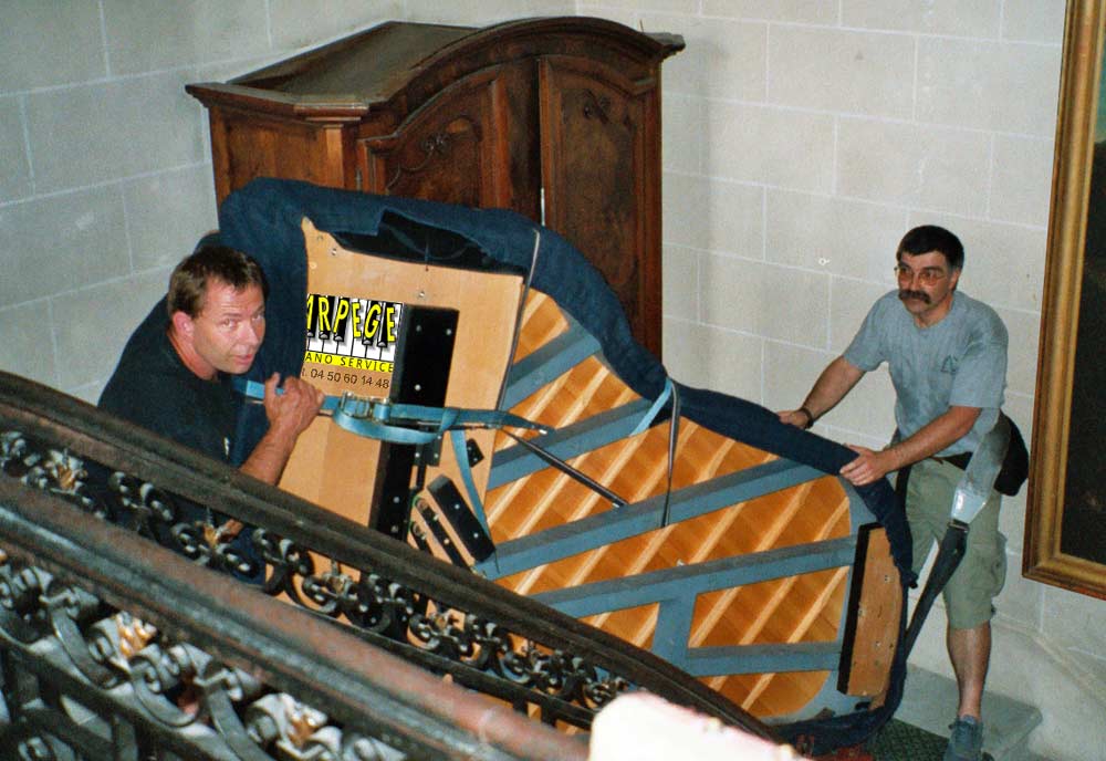 Transport, port d'un piano à queue dans cage d'escaliers d’apparat par 2 porteurs et des sangles de portage