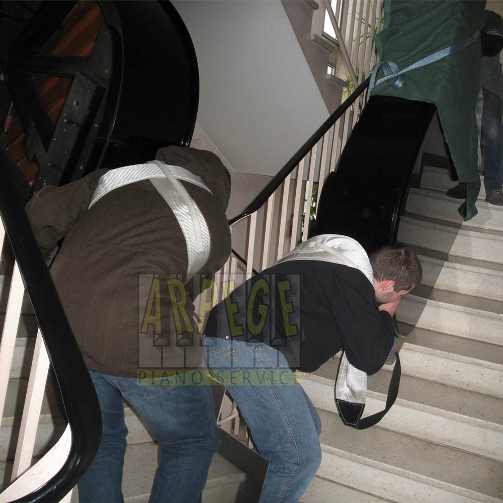 Transport, port d'un piano à queue dans cage d'escaliers par 2 porteurs et des sangles de portage